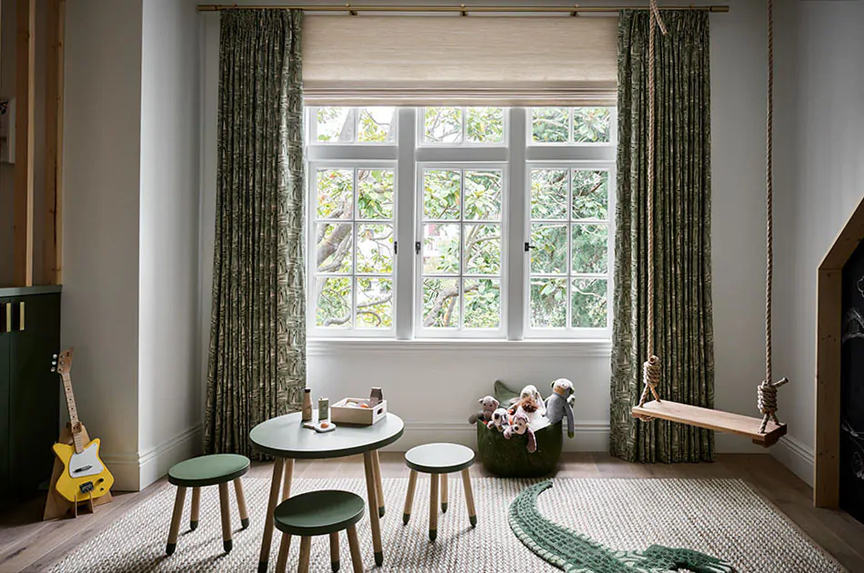 Kids curtains made of Tailored Pleat Drapery with a dark green leafy pattern add texture and warmth to a playroom