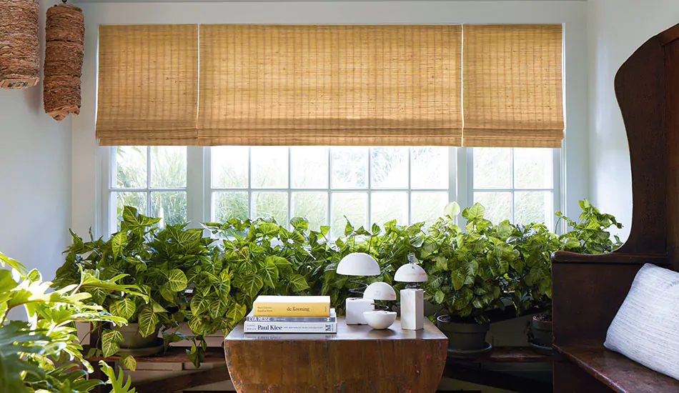 A bright sunroom features privacy shades in the Woven Wood Shade style made of Coastline material in Oat for a warm gold glow