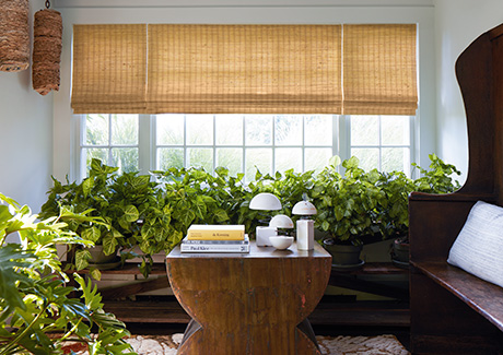 Waterfall Woven Wood Shades made of Coastline in Oat beautifully filter sunlight in a sunroom with lots of potted plants