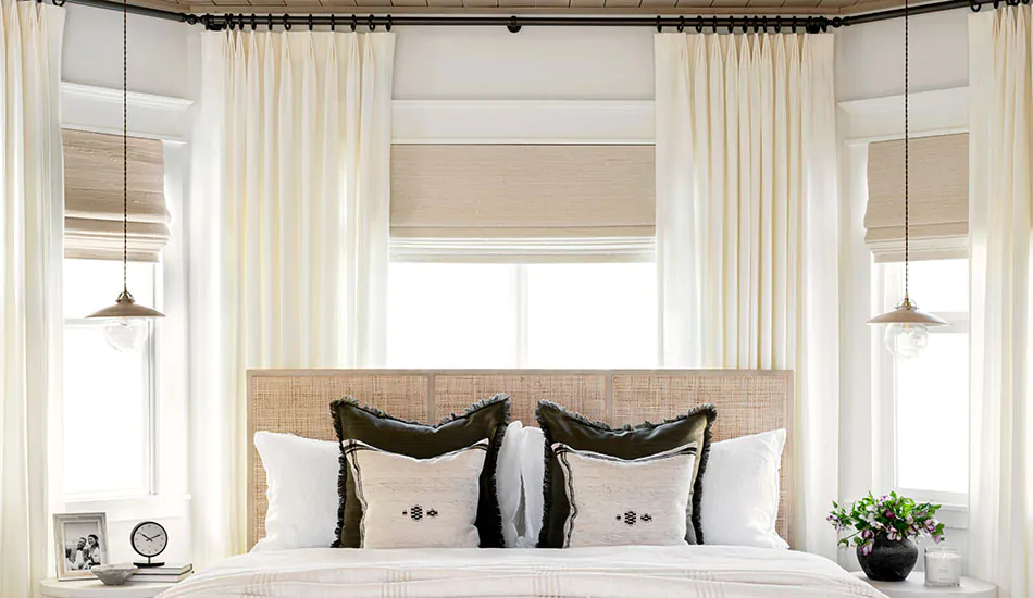Bay window curtains made of Linen in Ecru hang between windows which feature woven wood shades made of Bayshore in parchment