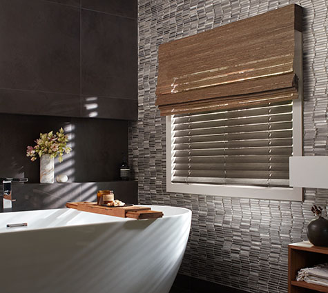 Layering styles, one of the window treatment trends 2024, is seen in this bathroom's Waterfall Woven Shades over Wood Blinds