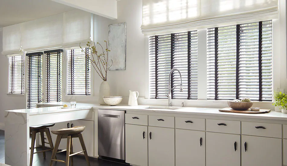A bright white kitchen features Wood Blinds made of Bamboo in Black for contrast and Roman Shades in a white color