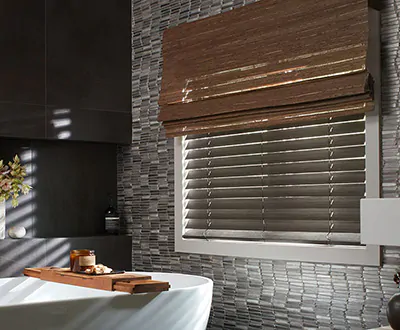 A small basement window in a bathroom features Wood Blinds made of Bamboo in Black and a woven shade made of Del Rey in Taupe