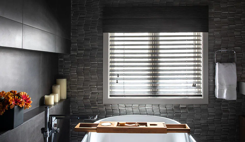 A dark calm bathroom has Wood Blinds made of 2-inch Bamboo in Black layered with a Woven Wood Shade made of Del Rey in Taupe