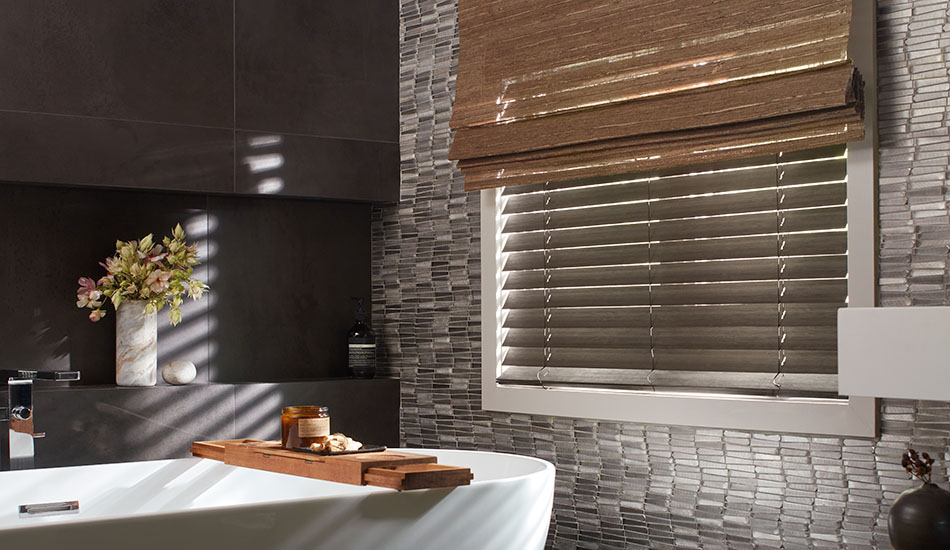 A dark calm bathroom has Wood Blinds made of 2-inch Bamboo in Black layered with a Woven Wood Shade made of Del Rey in Taupe as layered window coverings for adjustable privacy