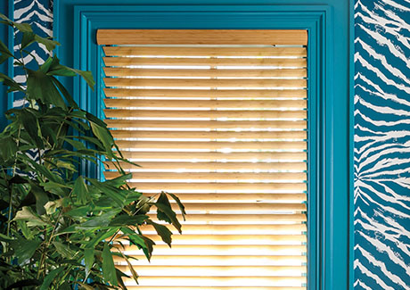A close up of Wood Blinds made of Bamboo in Natural show a light wood tone that complements the turquoise-painted walls