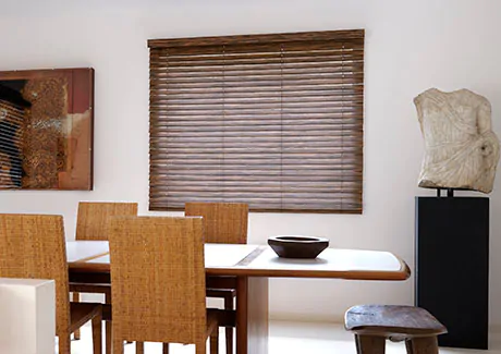A dining room with a mid-century modern aesthetic features wood furniture and 2-Inch Exotic Wood Blinds in Ebony
