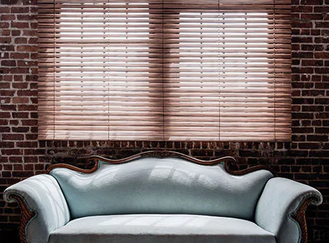 A red brick wall, a couch and wooden blinds offers inspiration for the best type of blinds for living rooms