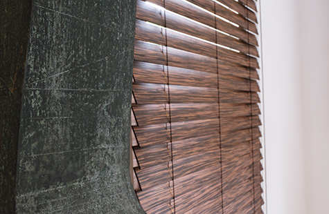 A piece of art stands next to a window with Exotic Wood Blinds in Zebrano which feature a realistic wood grain