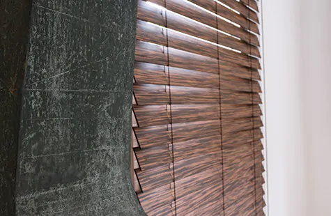 A piece of art stands next to a window with Exotic Wood Blinds in Zebrano which feature a realistic wood grain