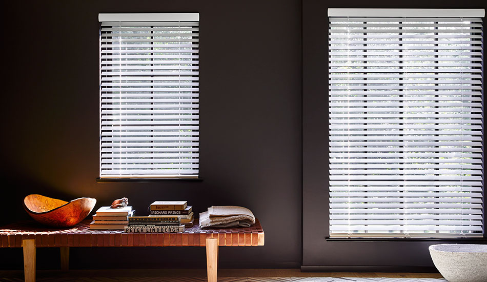 A room with dark grey walls and a wood bench has cordless Wood Blinds made of 2-inch Matte in Ivory to contrast the walls