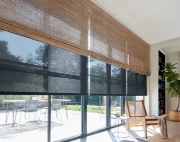 Waterfall Woven Wood Shades layered over Roller Shades hung on floor to ceiling windows with patio furniture outside
