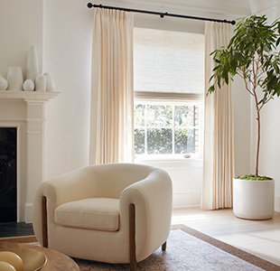 A living room features a Woven Wood shade in Harper, Ivory, layered with Tailored Pleat Drapery in Luxe Linen, Oyster