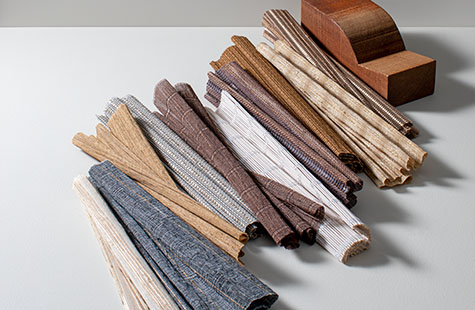 Woven Wood Shade swatches made of Artisan Weaves materials are folded in a line on a table with a decorative wood piece