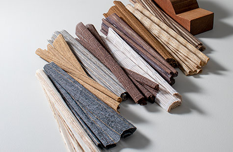 Woven shades swatches of the Artisan Weaves collection lay decoratively on a table with a wood sculpture