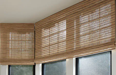 A bay window features Waterfall Woven Wood Shades made of Cove in Beige, layered over Solar Shades in a family room