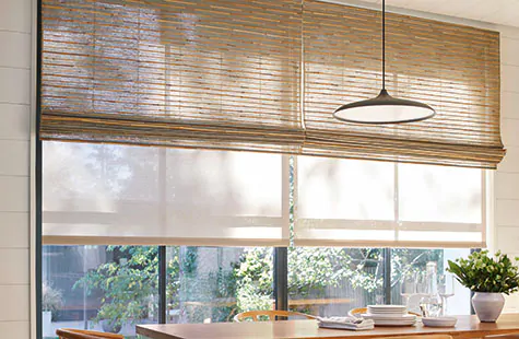 Woven Wood Shades made of Reed in Slate are used as window treatments for large windows in a boho-inspired dining room